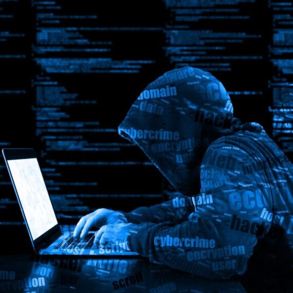 Hacker in a hooded jacket working on a laptop surrounded by digital code.